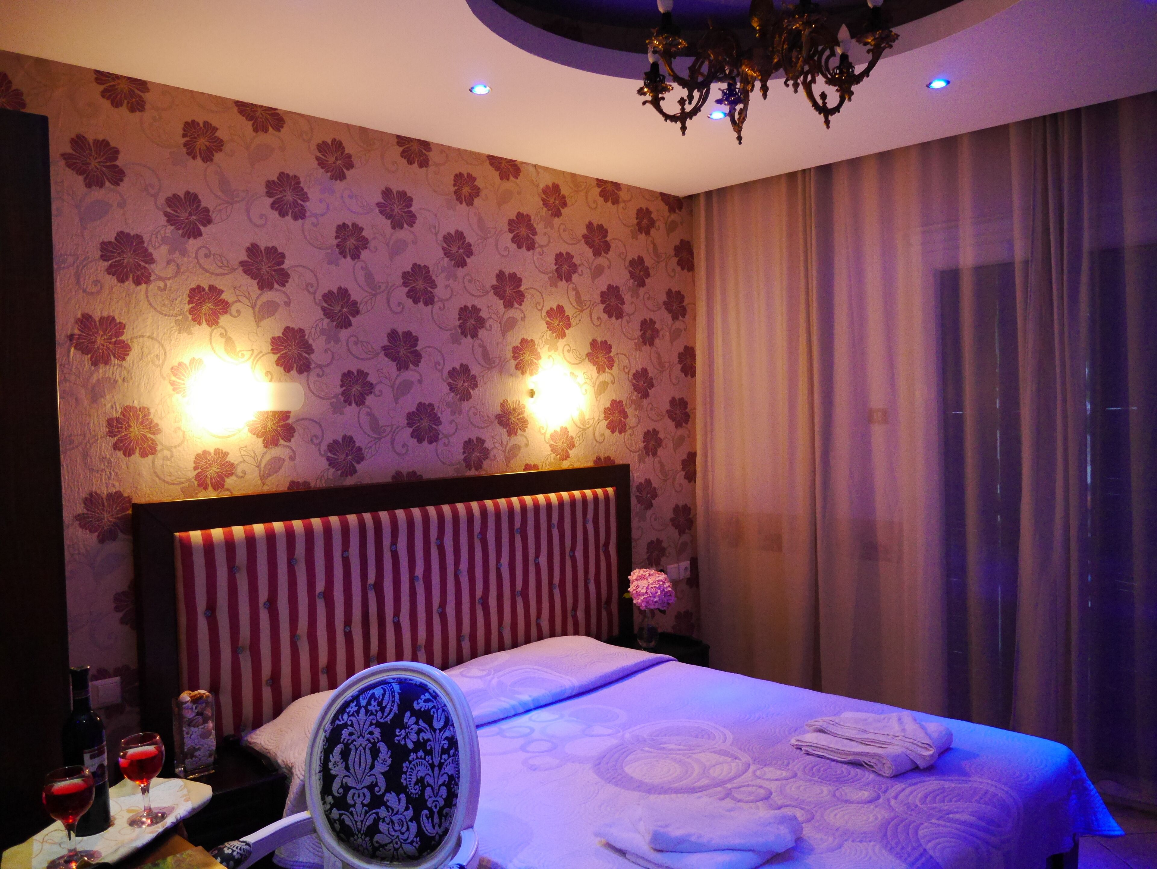 Habitación de hotel con cama, mesita de noche con lámpara, espejo y ventana con cortinas.