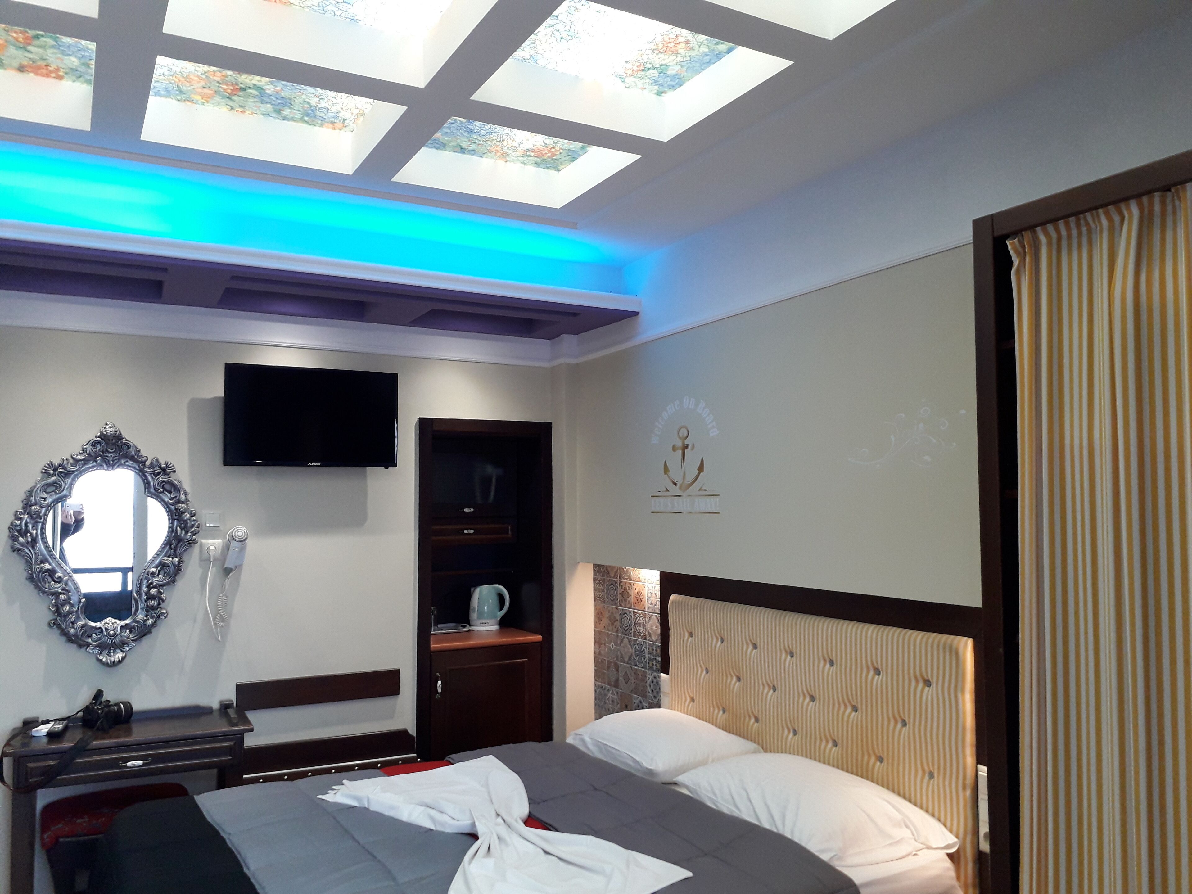 A hotel room with a bed, a TV, a mirror, a wardrobe, and a ceiling with skylights.