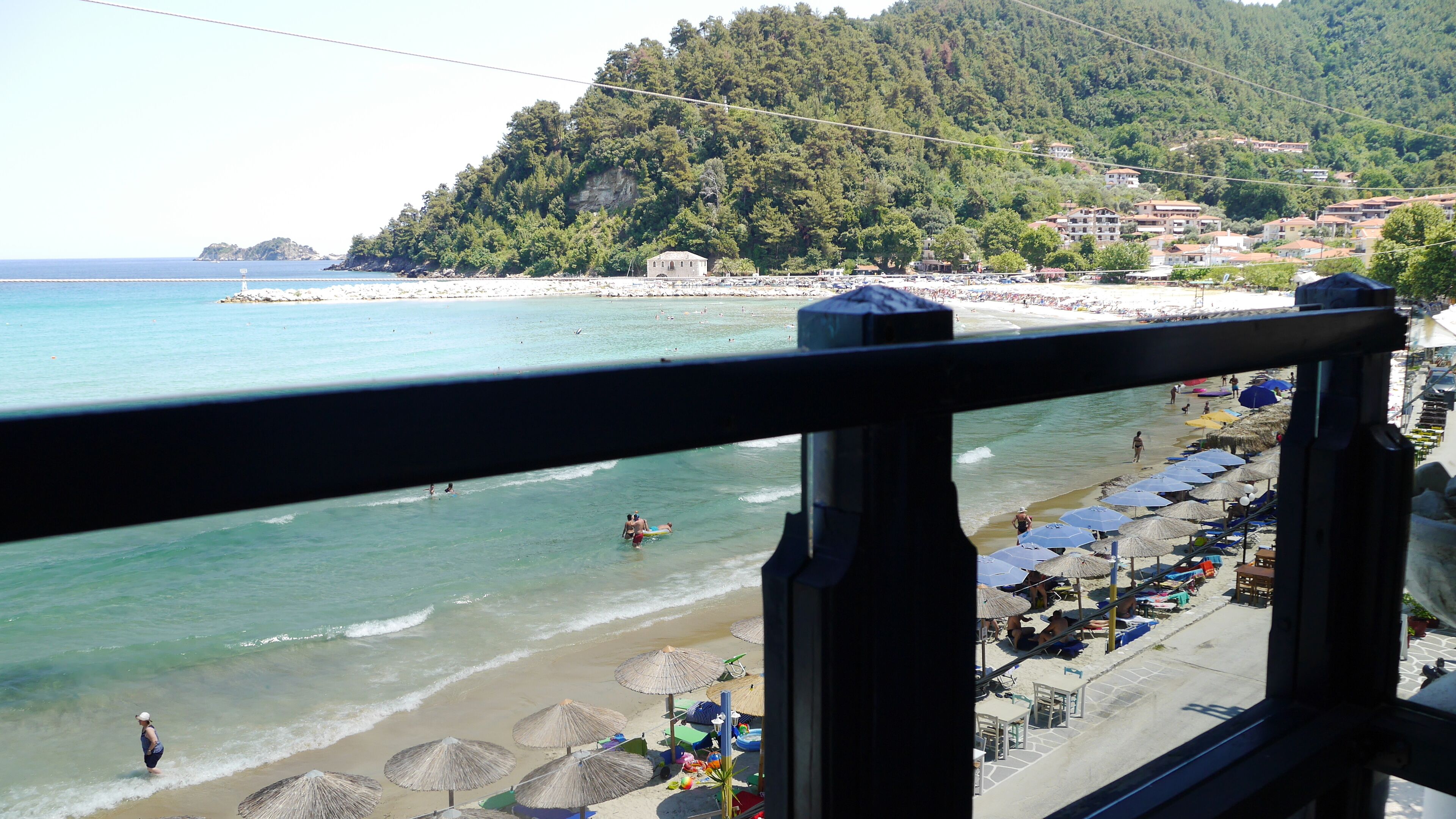 A beach with umbrellas and beach chairs, a clear view of the sea, and a hillside with buildings.
