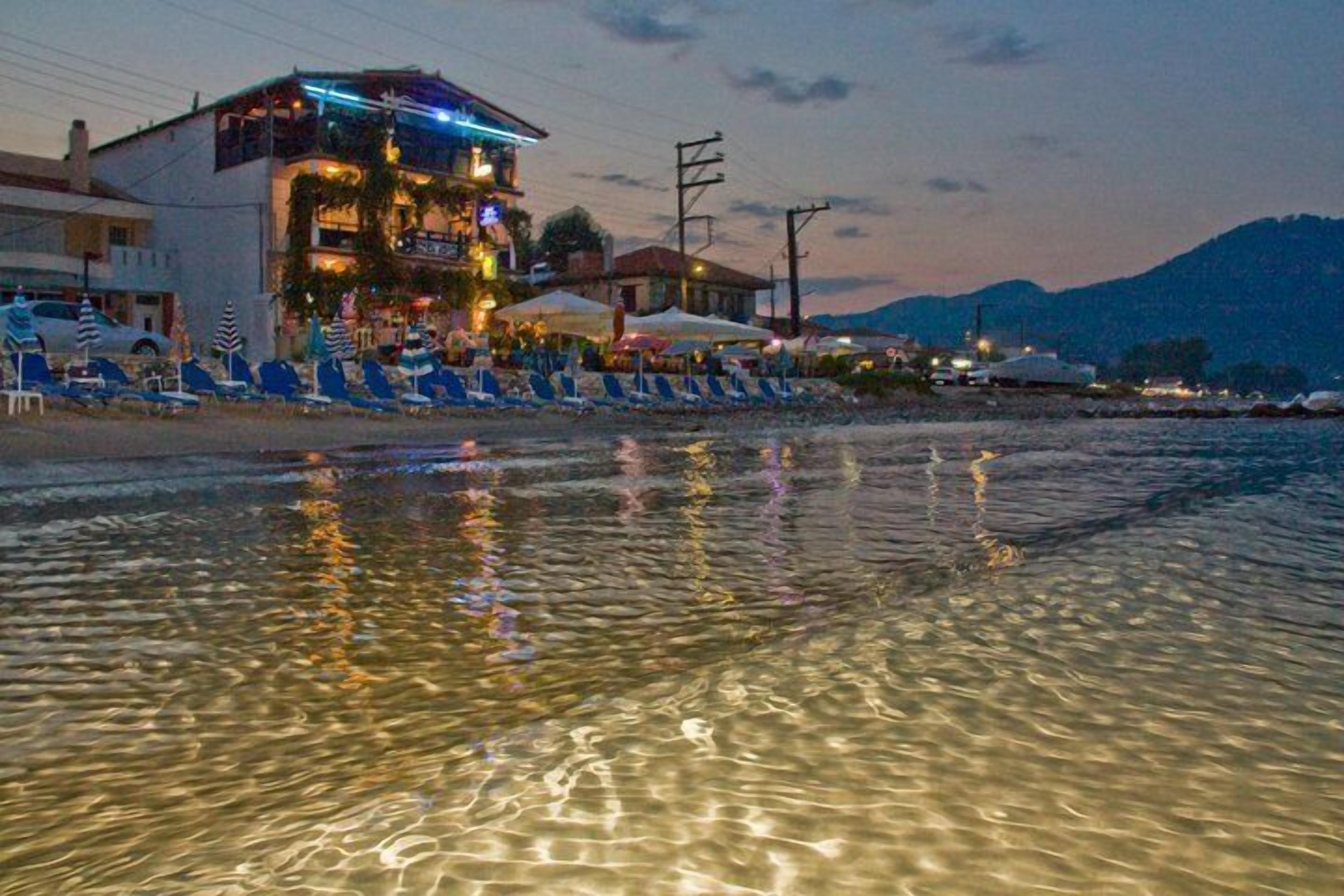 A beachfront hotel with clear waters reflecting the building and umbrellas.