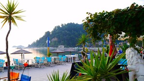 A beachside café with outdoor seating, a view of the sea, and a statue. - Blue Sea Beach Hotel (Thasos)