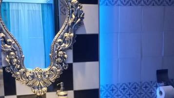 A bathroom with a checkered floor, a sink with a decorative mirror, a toilet, and a trash bin.