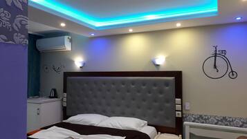 A bedroom with a tufted headboard, a bedside table, a wall-mounted bicycle decoration, and a ceiling with blue LED lighting.