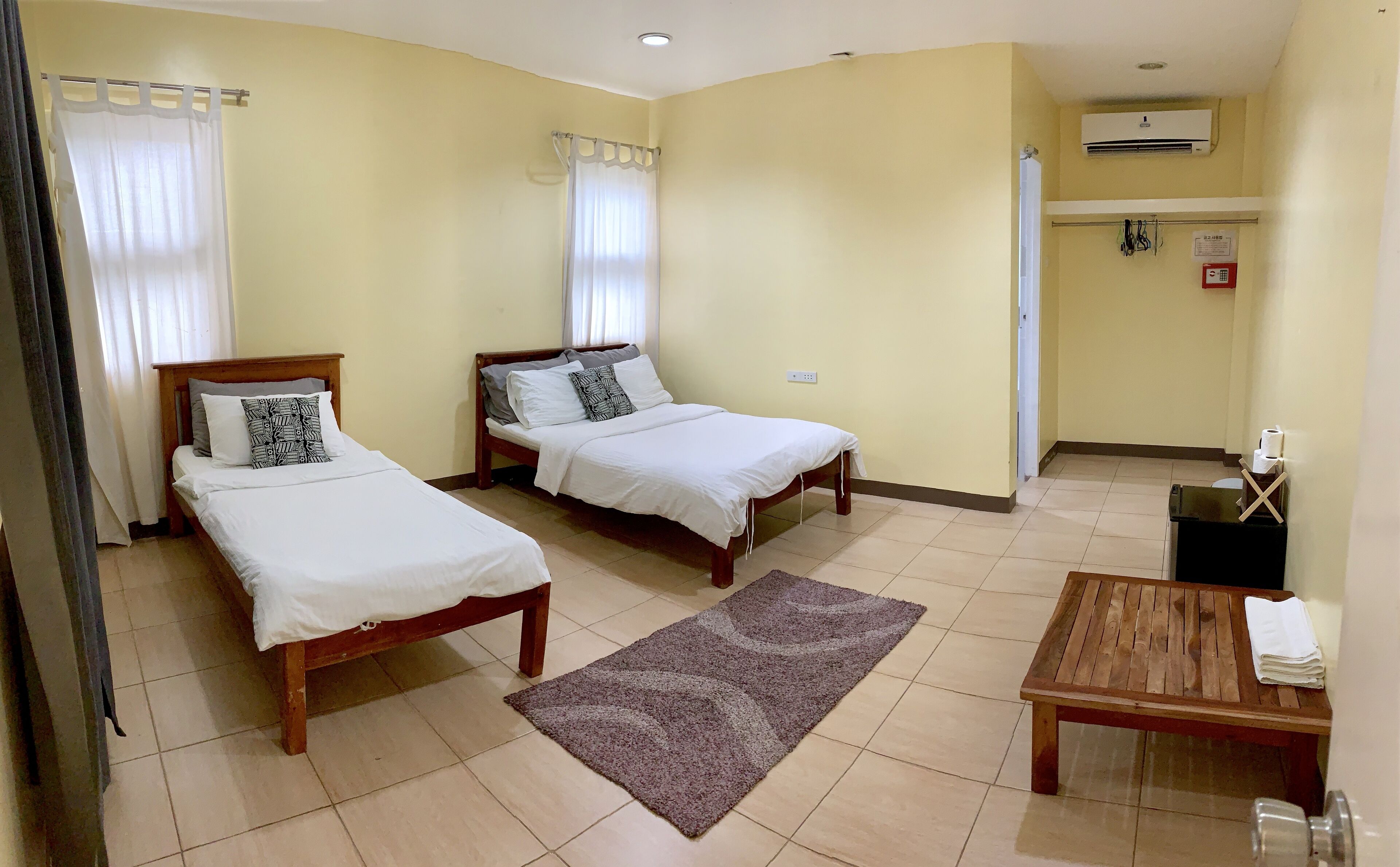 A hotel room with two beds, a small table, a rug, and an air conditioning unit.