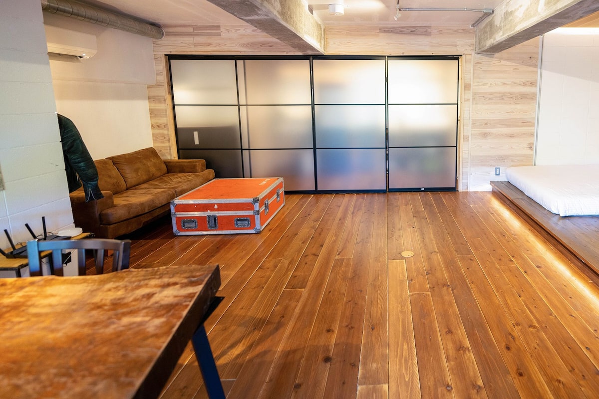 Een compacte kamer met een houten vloer, een bank, een bed en een schuifdeur met geëtste glaspanelen.