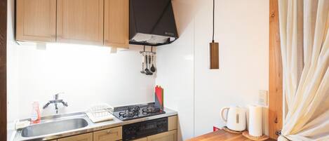 Cocina compacta con gabinetes de madera, un lavamanos de acero inoxidable, una estufa a gas y una campana extractora negra.