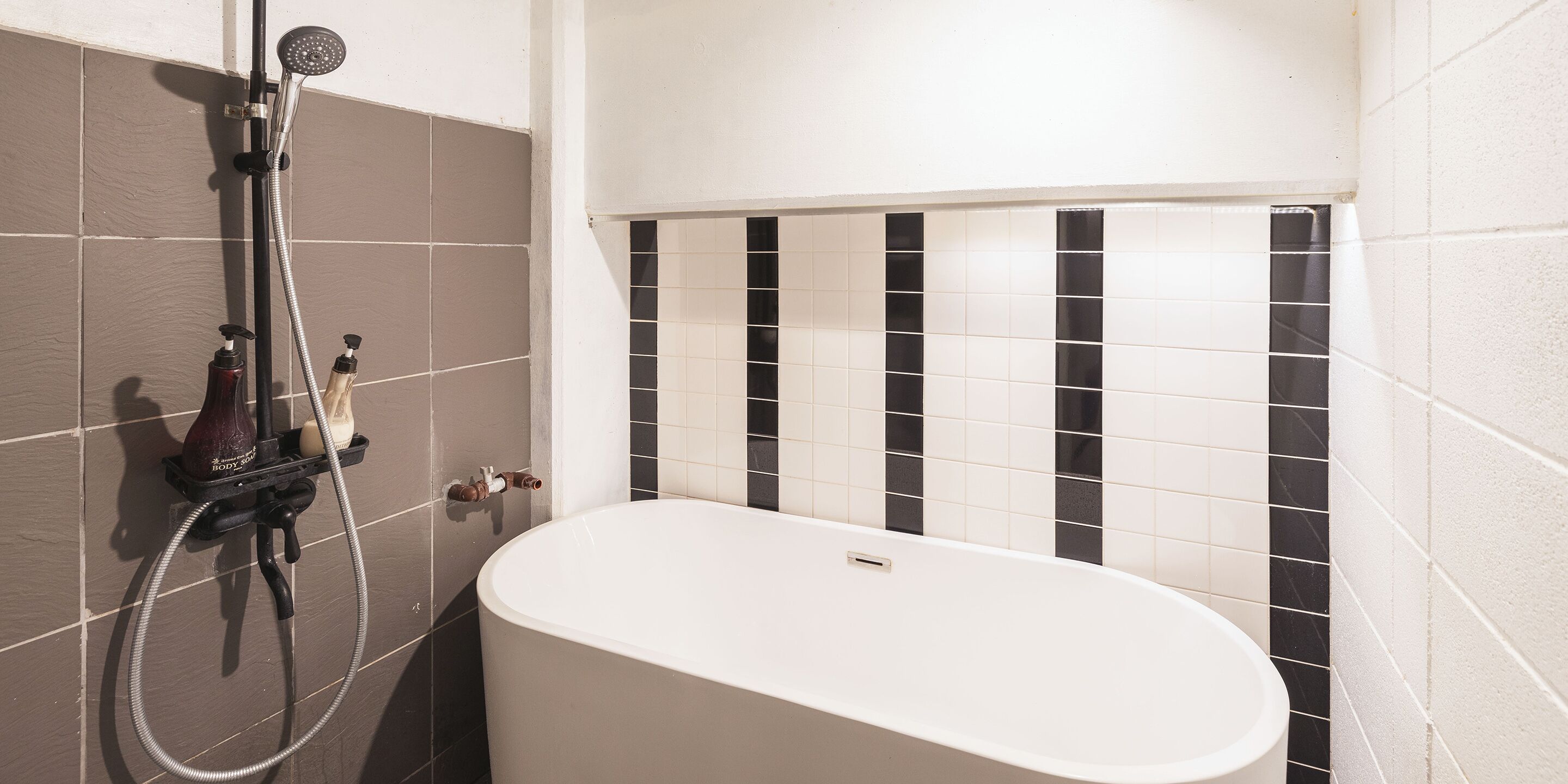 A bathroom with a bathtub, a showerhead, and a hand soap dispenser.