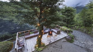 A wooden deck with outdoor seating and a fireplace, surrounded by lush greenery and a rocky path. - Springs Village Hakone Glamping Resort (Hakone)
