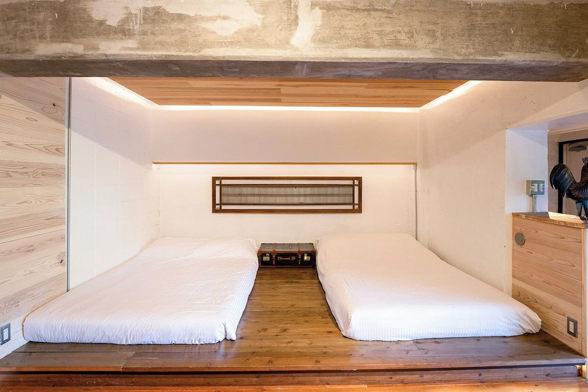 Een kamer met twee bedden, een houten vloer, een wandheater en een houten dressoir met een haanbeeld.