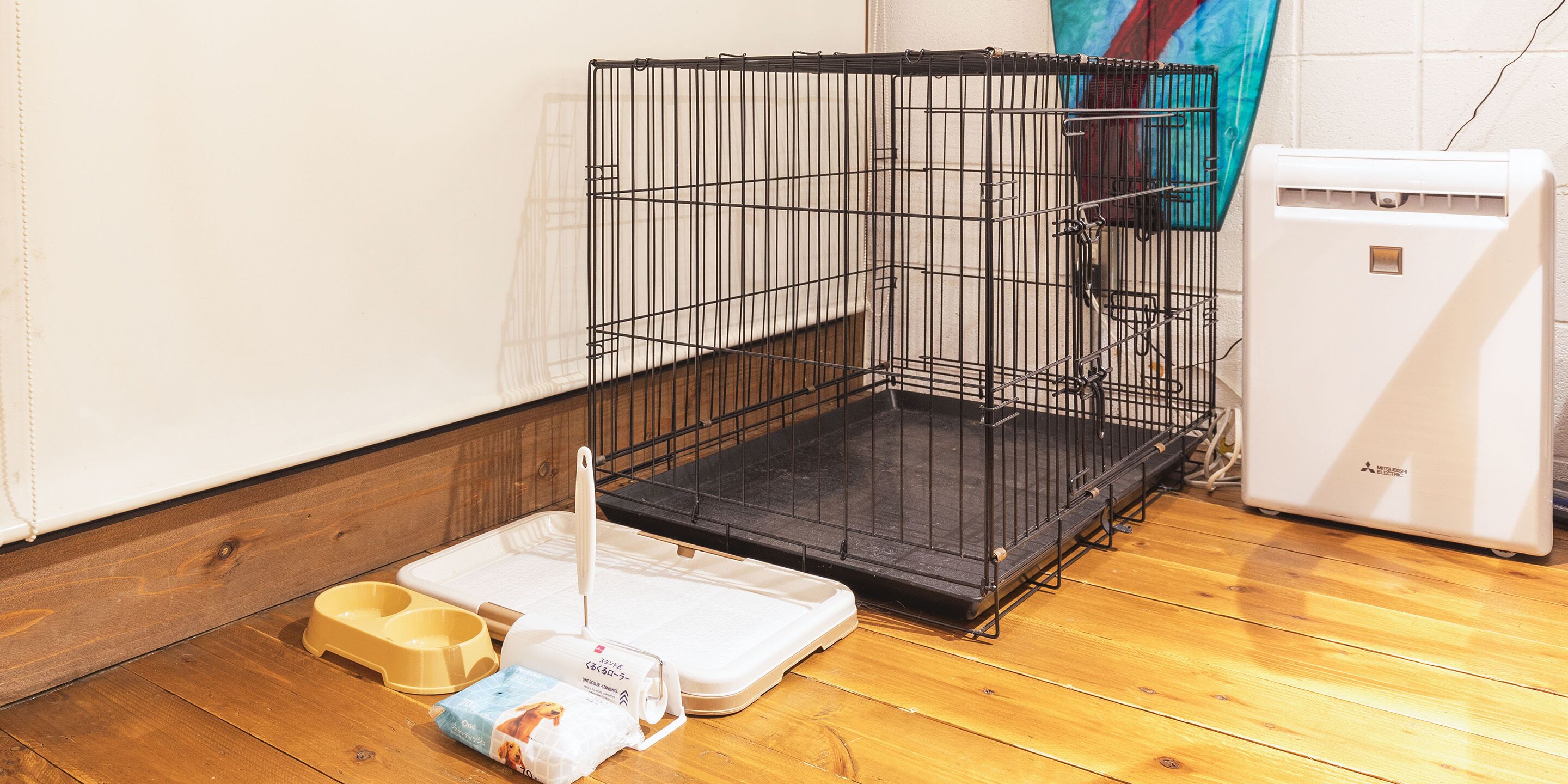 A pet cage with a white heater, a food bowl, and a litter box on a wooden floor.