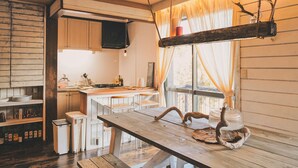 A rustic kitchen with wooden cabinets, a wooden dining table, and a hanging light fixture. - Springs Village Hakone Glamping Resort (Hakone)