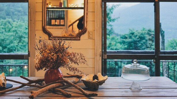 A wooden table with a vase of dried flowers, a decorative skull, and a glass cake stand. - Springs Village Hakone Glamping Resort (Hakone)