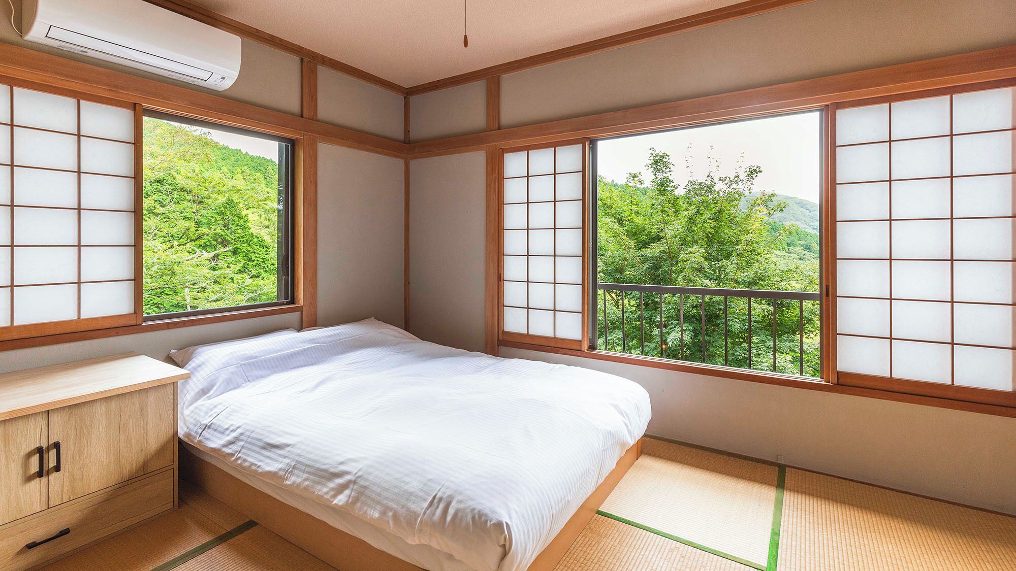 Une pièce de style japonais traditionnel, avec un sol recouvert de tatamis, un lit, un bureau en bois et de grandes fenêtres équipées de panneaux coulissants en papier de riz (shoji).