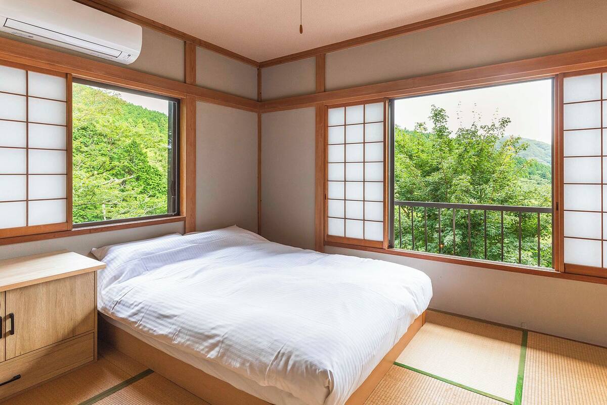 Een traditionele Japanse kamer met tatami vloerbedekking, een bed, een houten bureau en grote ramen met shoji schermen.