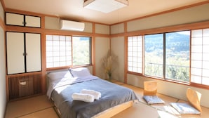 A traditional Japanese-style bedroom with tatami flooring, a bed with a gray blanket, a wooden wardrobe, and large windows offering a view of the outdoors. - Springs Village Hakone Glamping Resort (Hakone)