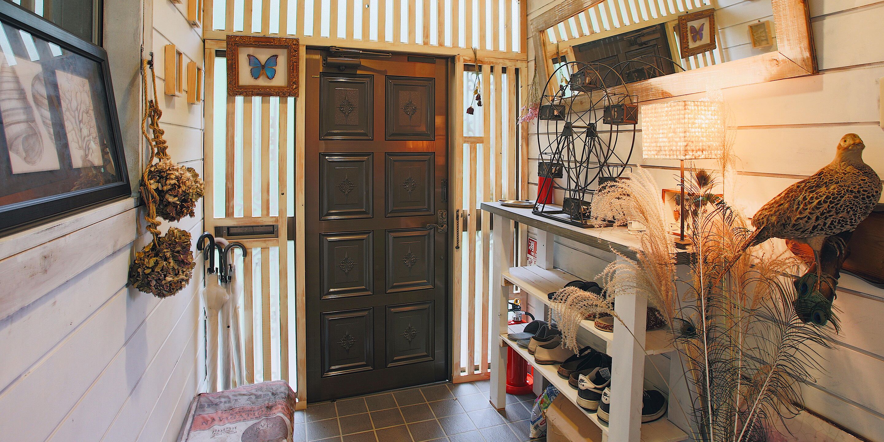 Een smalle gang met een houten deur, een plank met schoenen en een pauwdecoratie.