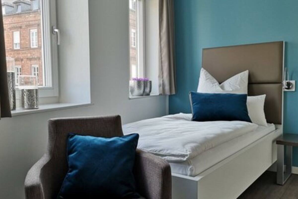 Une chambre d’hôtel avec un lit, une chaise, une table de chevet et une fenêtre avec des rideaux.