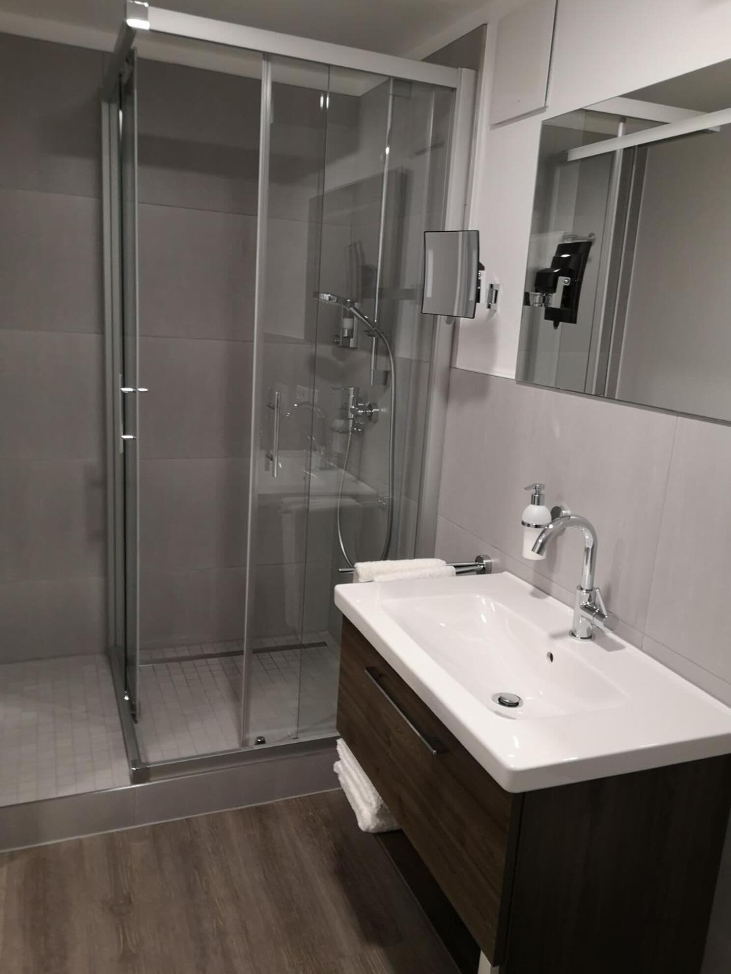 A modern bathroom with a glass-enclosed shower, a wooden vanity, and a large mirror.