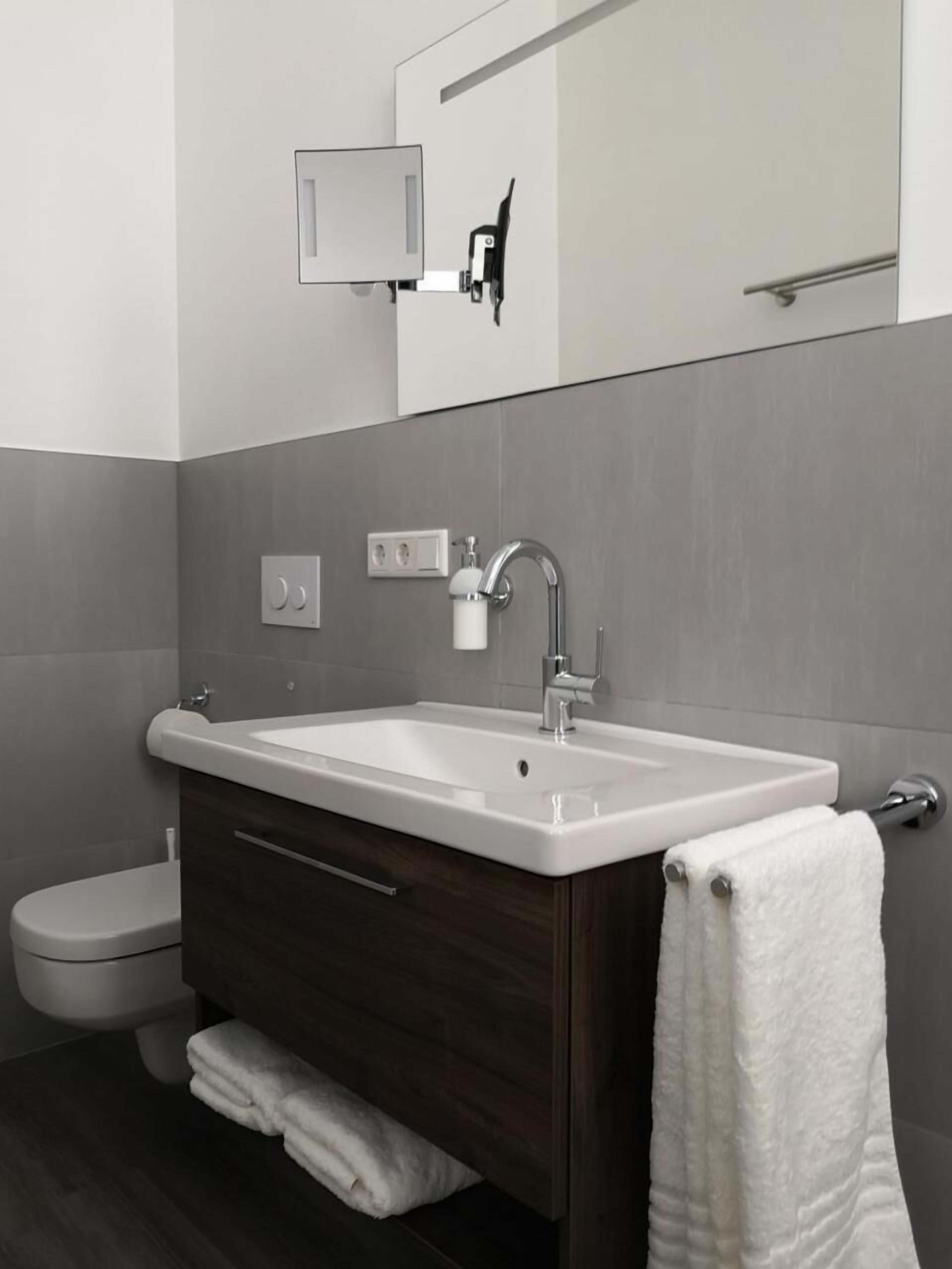 A modern bathroom with a white sink, dark wooden vanity, and a towel hanging on the wall.