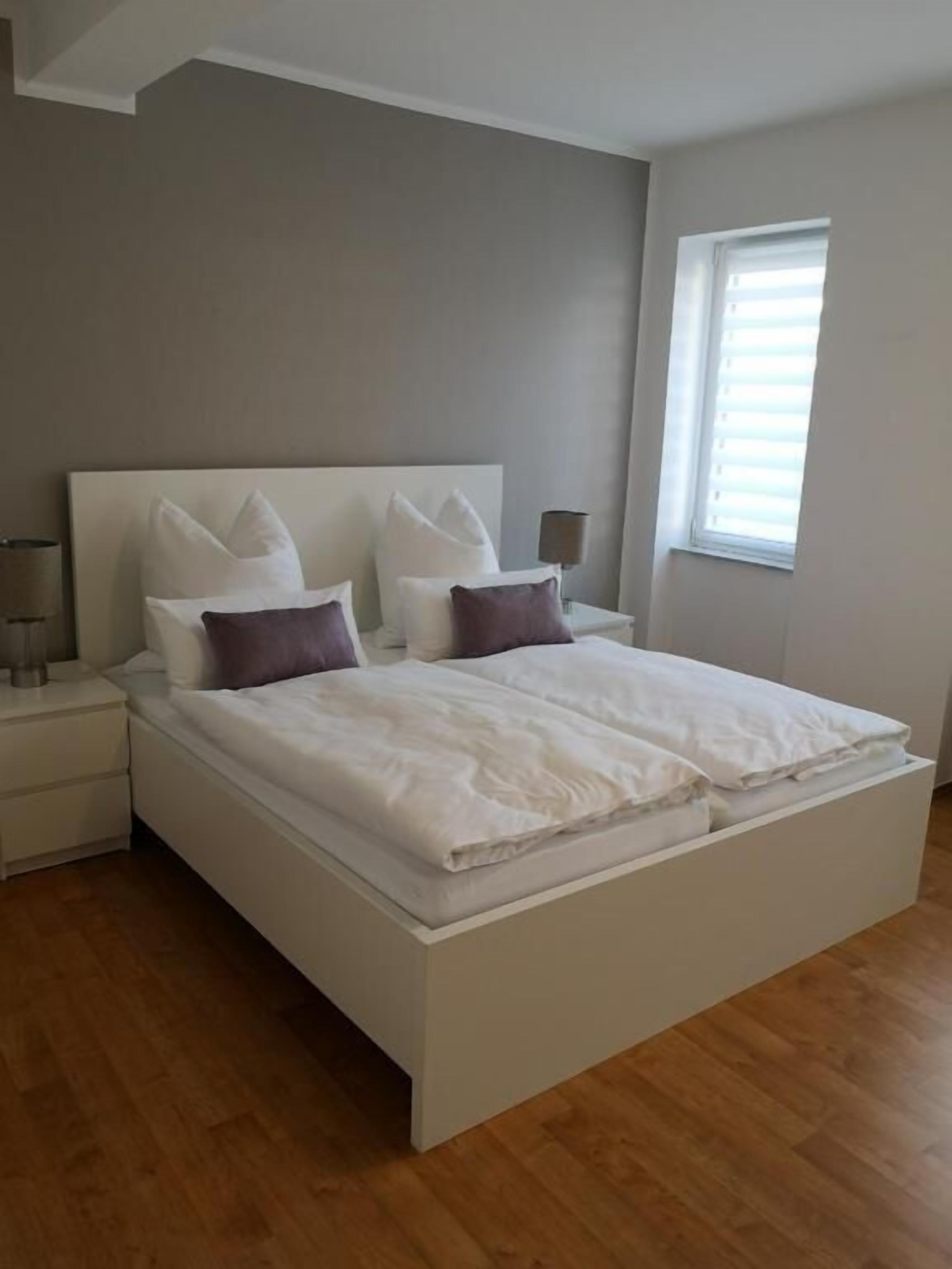 A modern bedroom with a large bed, two bedside tables, and a window with blinds.