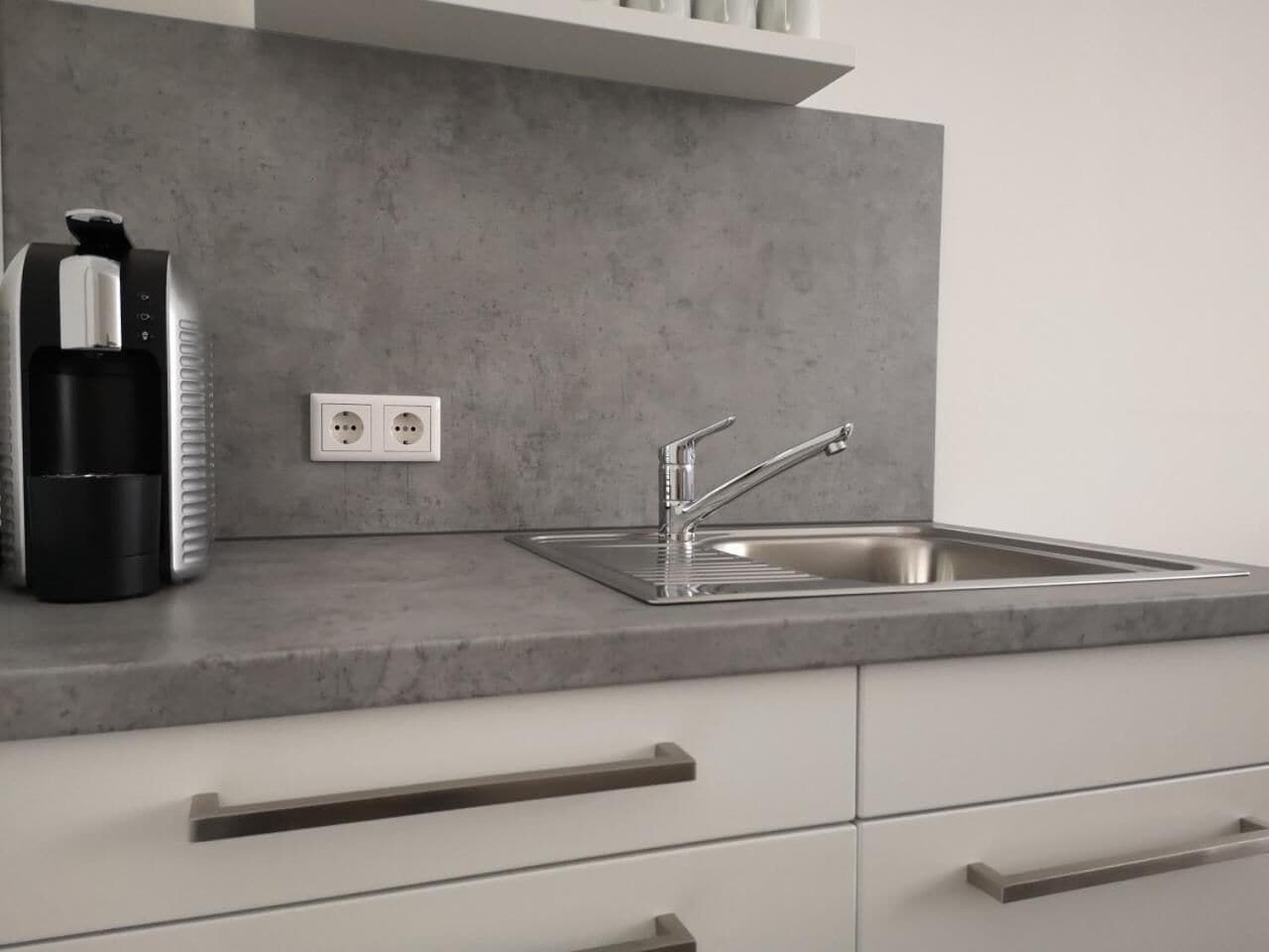 A kitchen with a stainless steel sink, a coffee maker, and a power outlet.