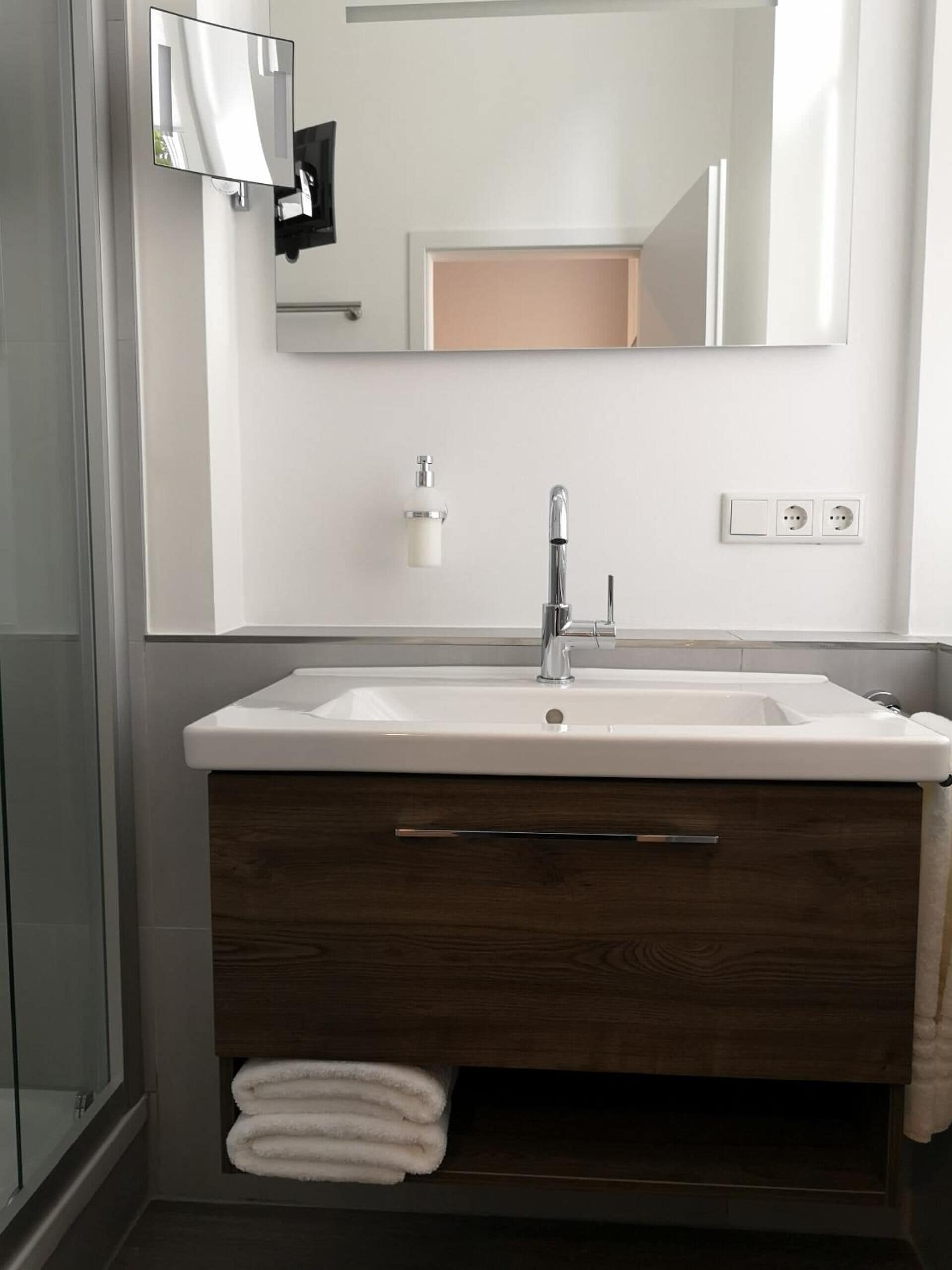 Un bagno con un lavandino bianco, uno specchio sopra e un portascopevoli con asciugamani.