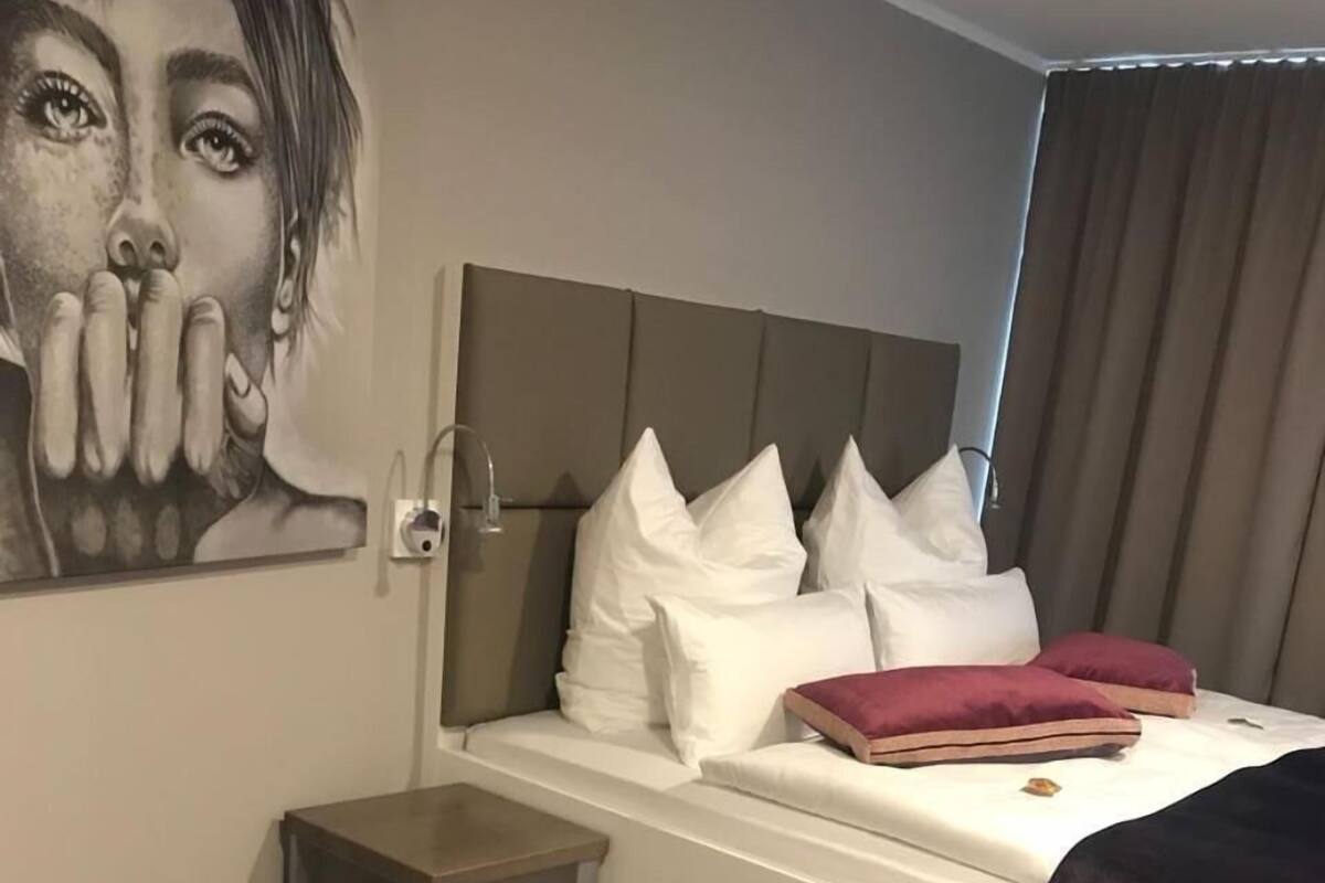 Une chambre à coucher moderne avec un grand lit, une petite table de chevet, un tapis à motifs et une œuvre d’art accrochée au mur.
