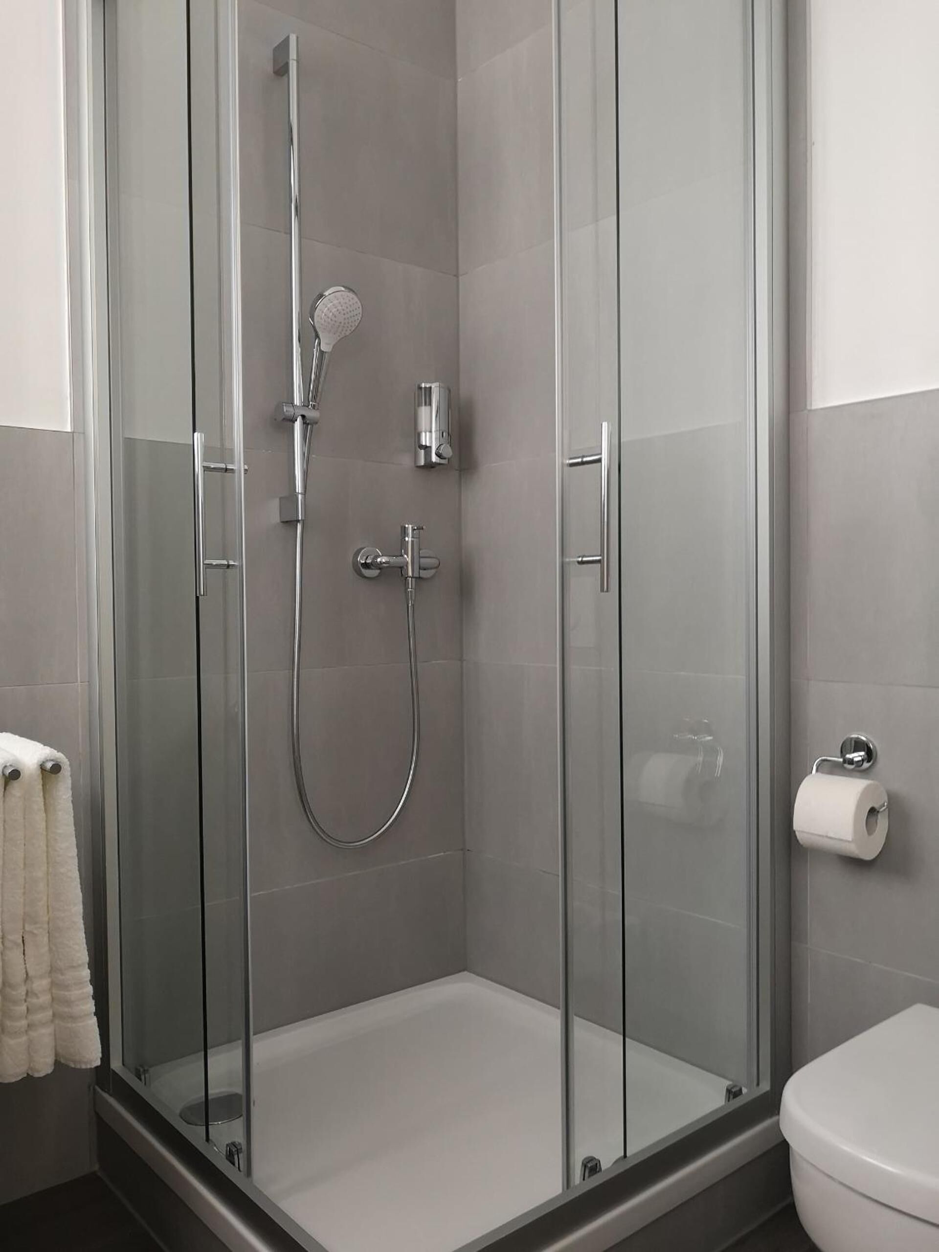 A glass-enclosed shower with a handheld showerhead and a wall-mounted faucet.