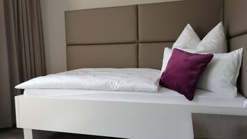 Un lit moderne doté d’une tête de lit rembourrée, de draps blancs et d’un coussin décoratif violet.