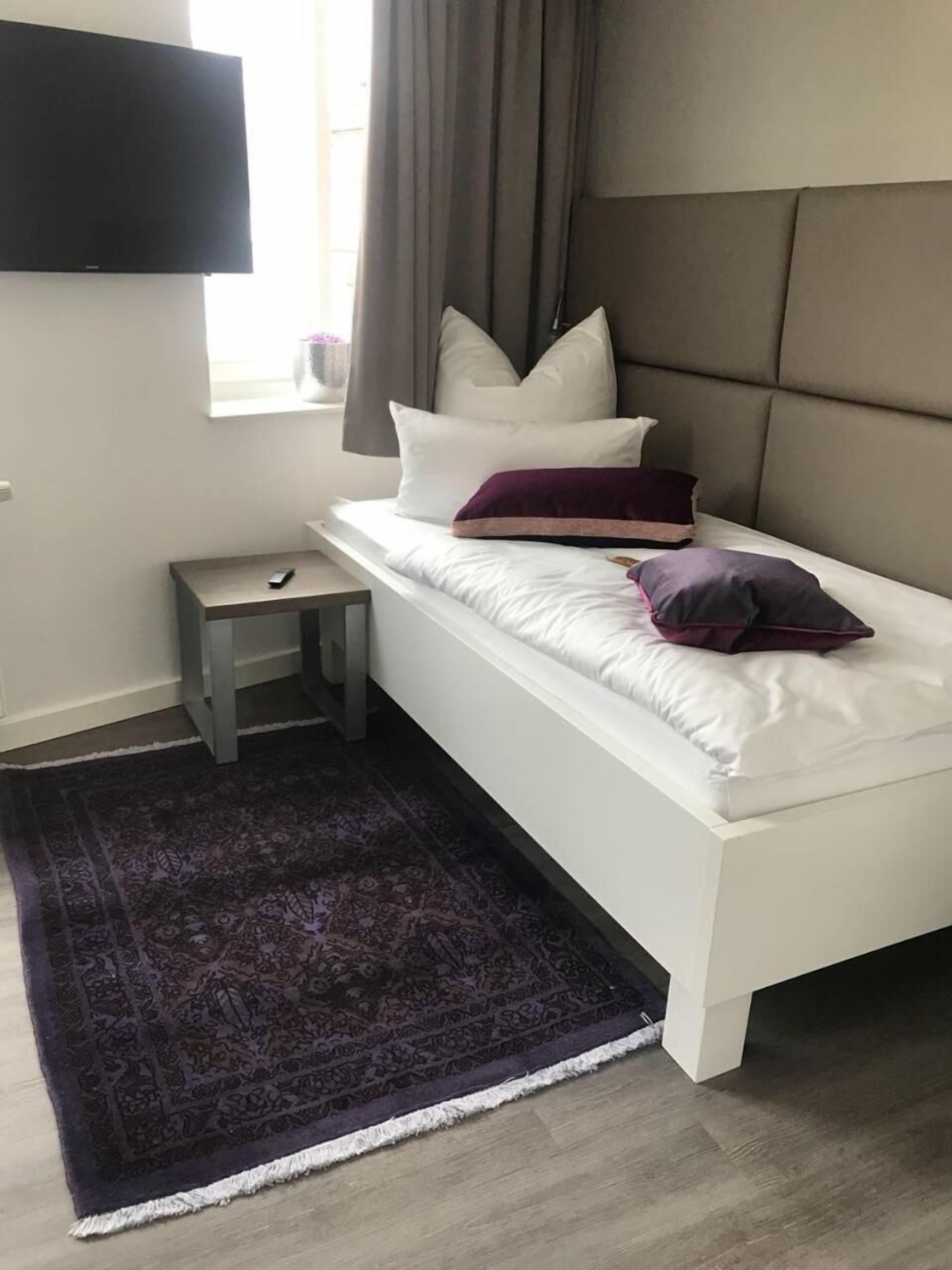 Un dormitorio con cama, mesita de noche, televisor y ventana con cortinas.