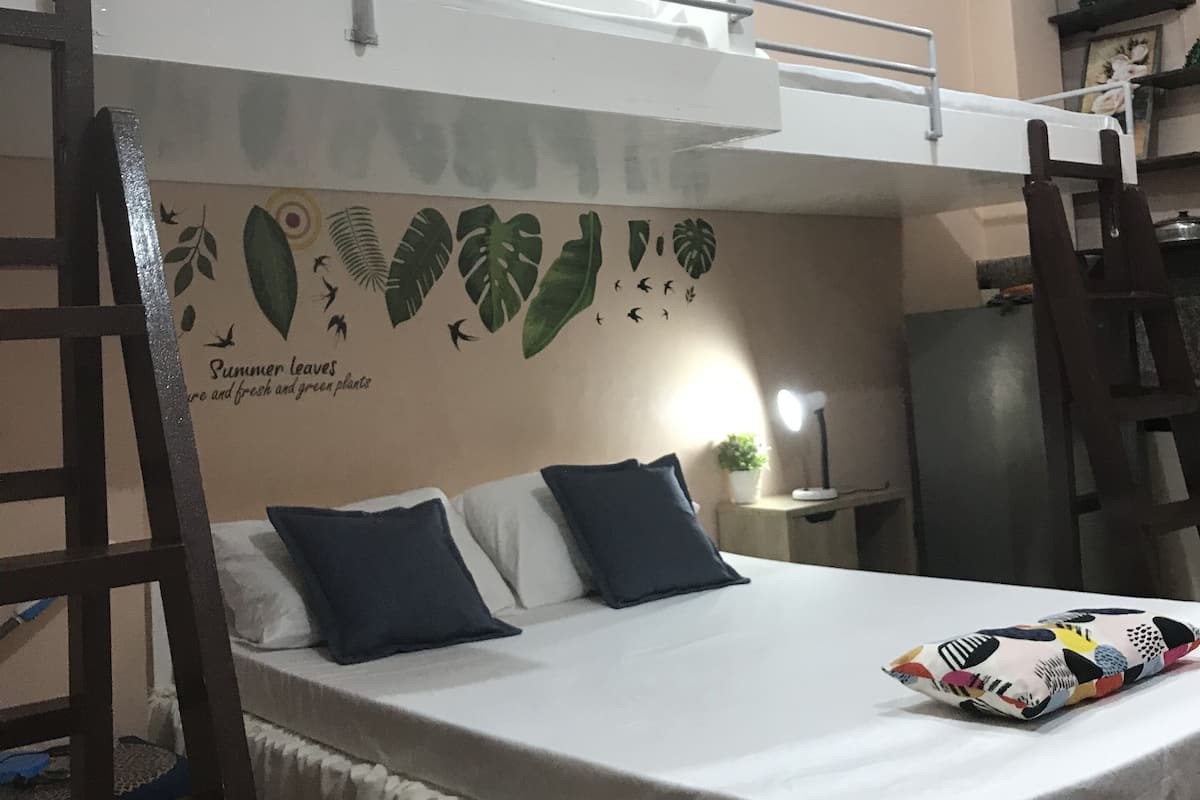 A bunk bed with a mural of leaves and birds on the wall, a small table with a plant, and a refrigerator in the background.