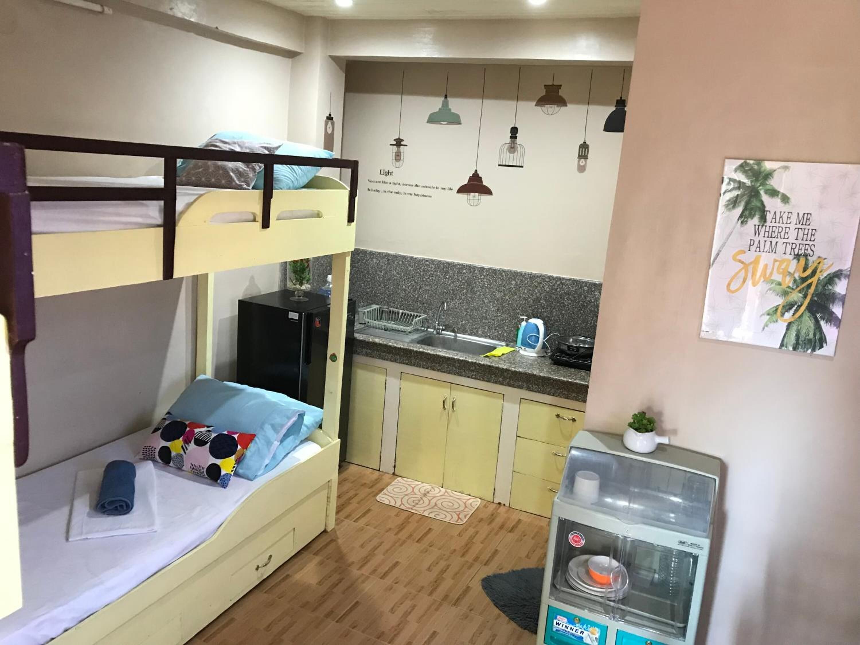 Quarto compacto com beliches, cozinha americana e pequena geladeira.