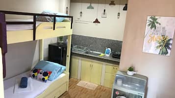 Quarto compacto com beliches, cozinha americana e pequena geladeira.