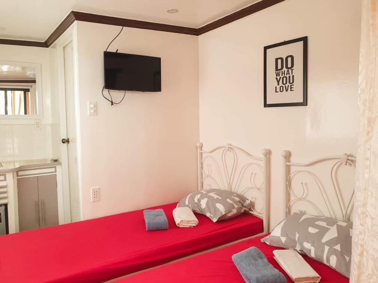 Habitación individual con una colcha roja, un televisor montado en la pared y un cartel motivacional.
