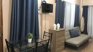 A living room with a sofa, a TV mounted on the wall, a wooden cabinet, and a glass table with chairs. - Palompon Traveler's Lodge (Palompon)