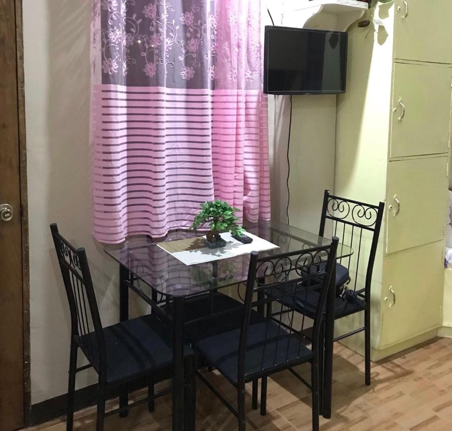 A small dining area with a table, chairs, a potted plant, and a television mounted on the wall.