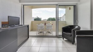 Un balcon avec une porte-fenêtre coulissante, une petite table avec des chaises, un canapé et un téléviseur posé sur un meuble.