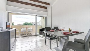 Un espace repas moderne avec une table et des chaises, un petit coin cuisine équipé d’un réfrigérateur, et une porte-fenêtre coulissante donnant sur une terrasse extérieure.