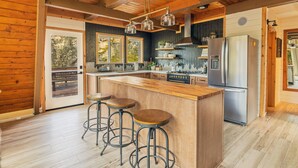 A modern kitchen with a wooden island, bar stools, stainless steel appliances, and large windows. - Cozy A Frame Cabin, Bass Lake, Ca-Acorn Falls  (Bass Lake)