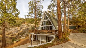 A modern, triangular-shaped cabin with a wooden balcony, surrounded by tall pine trees and rocky terrain. - Cozy A Frame Cabin, Bass Lake, Ca-Acorn Falls  (Bass Lake)
