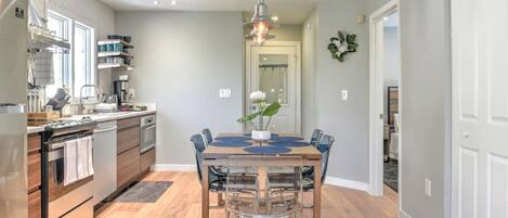 Una cocina moderna con comedor, que incluye una isla central, electrodomésticos de acero inoxidable y una lámpara colgante.