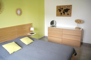 A bedroom with a bed, bedside table, lamp, dresser, and a world map on the wall.