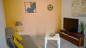 A living room with a sofa, a coffee table, a TV on a wooden stand, and a lamp.