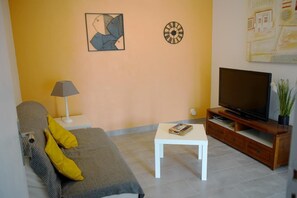 A living room with a sofa, a coffee table, a TV on a wooden stand, and a lamp.