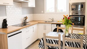 A modern kitchen with white cabinetry, a built-in oven, a coffee machine, and a window above the sink.