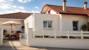 A two-story house with a white exterior, a red-tiled roof, and a white fence.