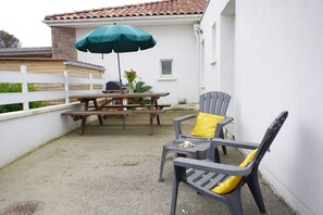 A patio with a table and chairs, a green umbrella, and a white building in the background. - Pleasant T3 house, all comforts, 300 m from beaches - Air conditioning & Wifi (Mimizan)