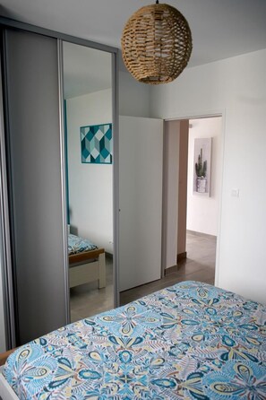 A bedroom with a bed, a wardrobe, a hanging light fixture, and a door leading to another room.
