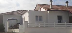 Uma casa de dois andares com fachada branca, telhado ladrilhado e cerca branca.