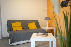 A room with a grey sofa, two yellow cushions, a white side table with a lamp, and a small table with a board game. - Pleasant T3 house, all comforts, 300 m from beaches - Air conditioning & Wifi (Mimizan)
